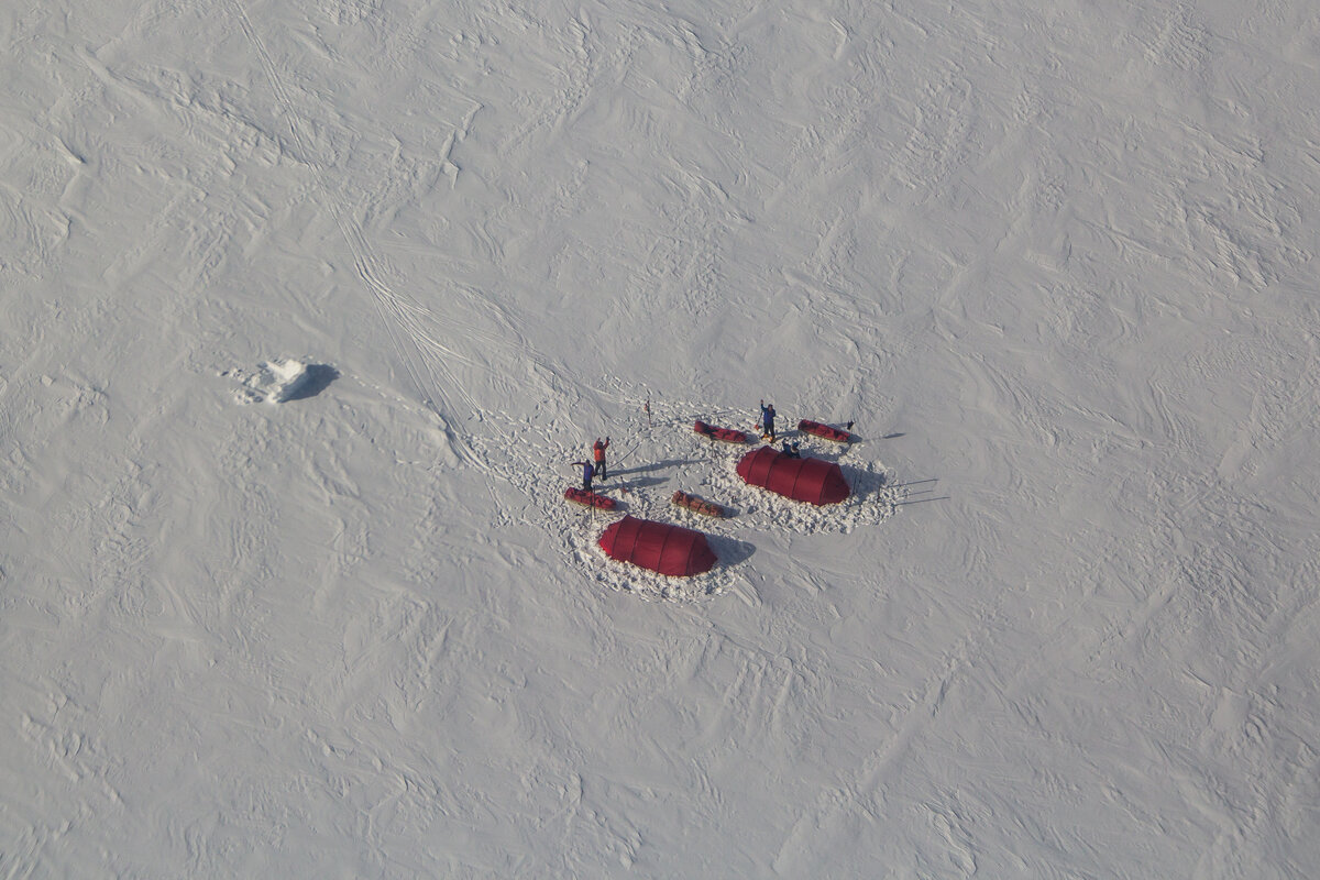 Ski team waves to a passing aircraft from field camp